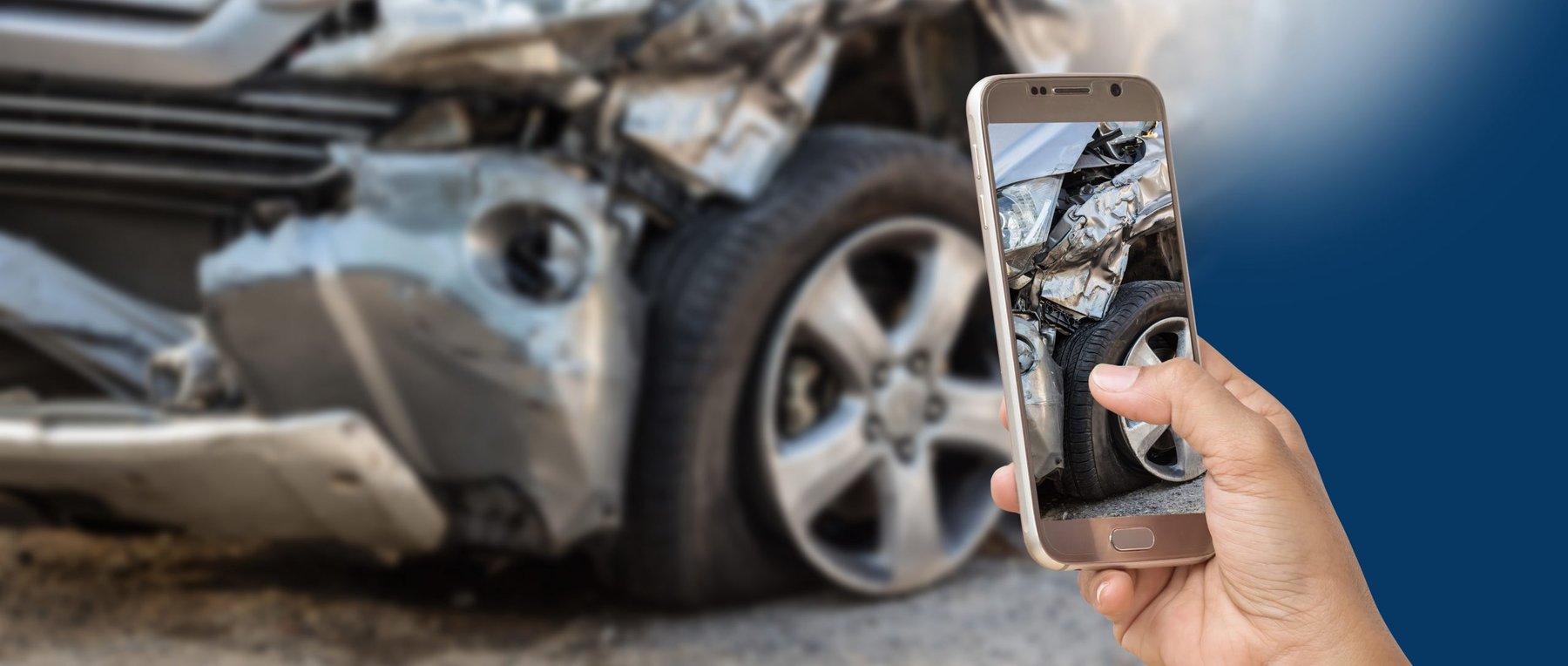 A hand holding a phone photographing a crashed car for remote damage assessment